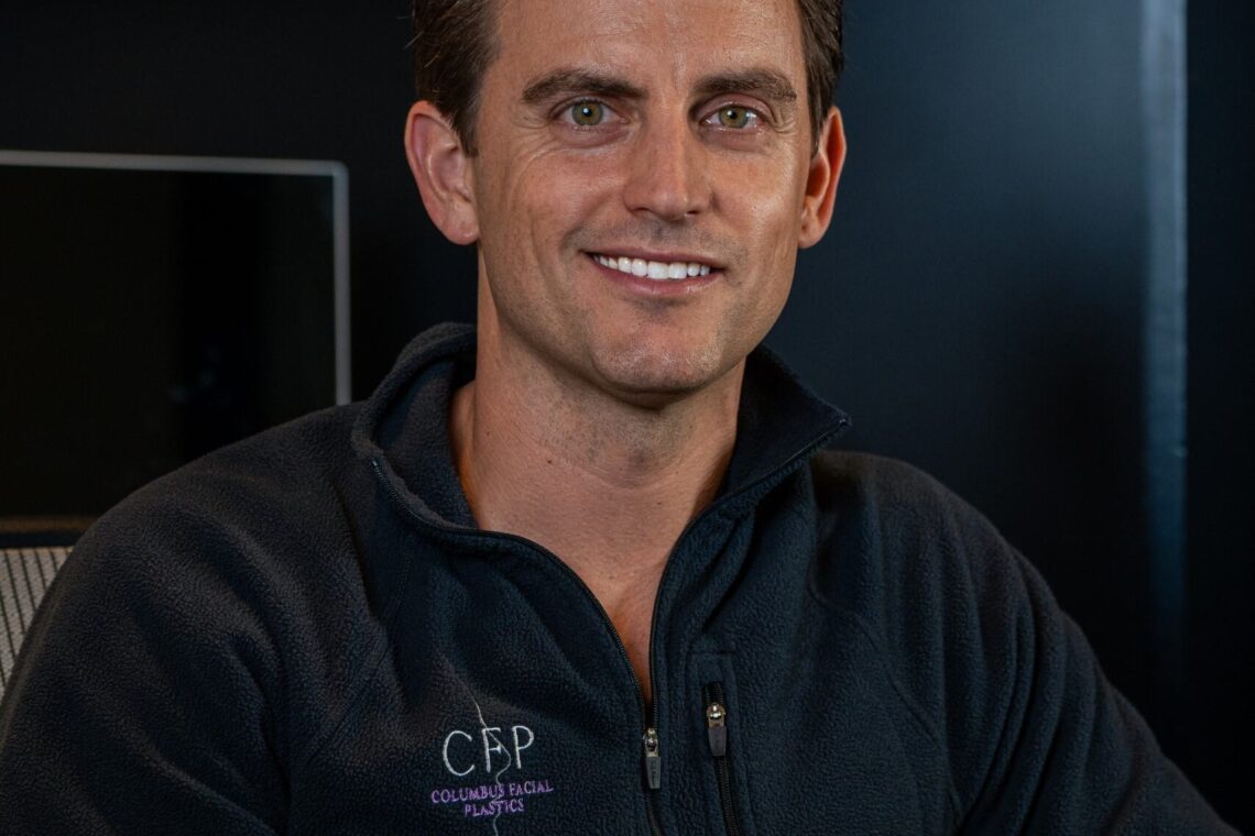 A man, smiling, sits with his hands folded